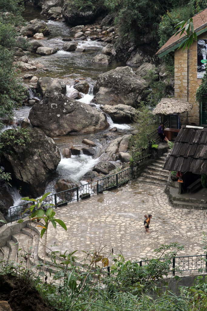 A young girl carries a baby on her back near a waterfall in Sapa, Vietnam.